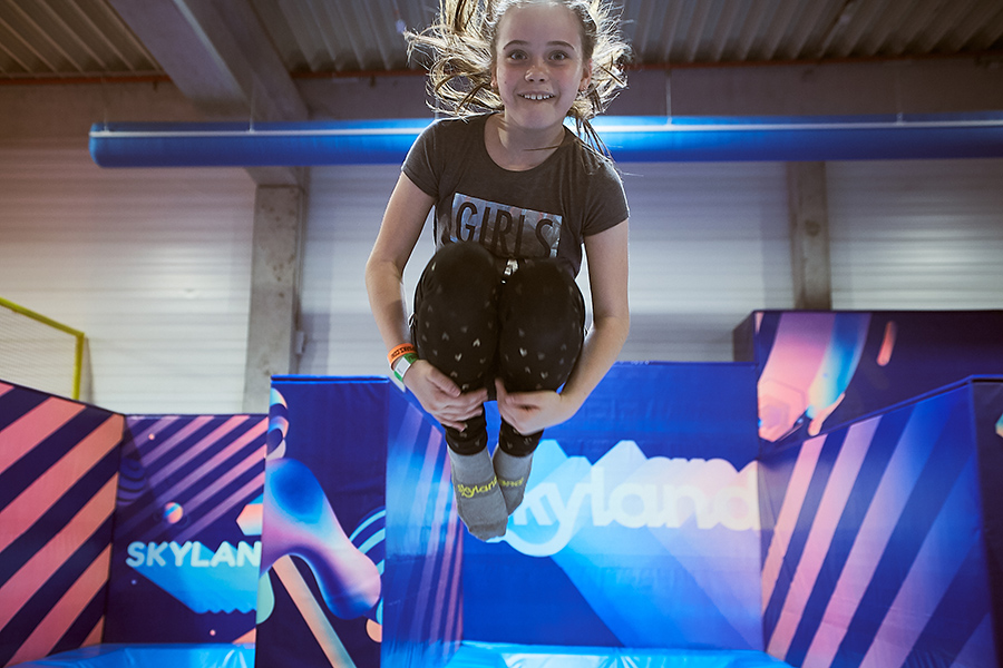 Eseményfotózás a SkyLand trambulin- és élményparkban. Csúszdák, trambulinok és sok más, amin a gyerekek ugrálni, csúszni, játszani tudnak. A fotón egy lány épp felugrik és a levegőben van.